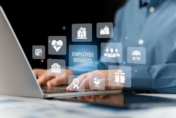 Person typing on a laptop with floating digital icons representing employee benefits like healthcare, rewards, and team support management