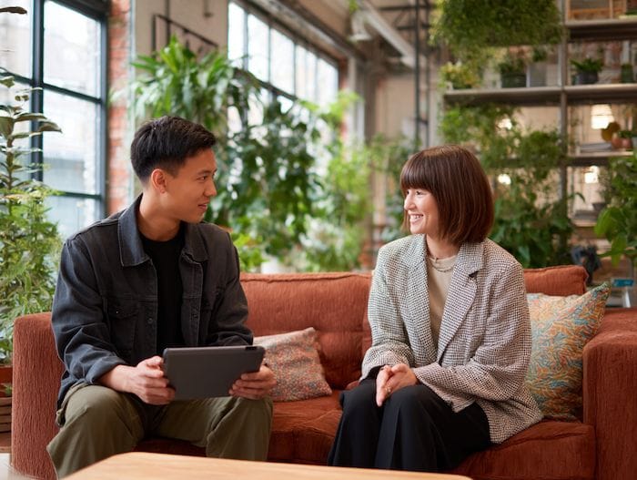 Two SME decision makers having a friendly discussion on a sofa in a modern office space